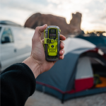 Campeur tenant un personal locator beacon ACR ResQLink View RLS à côté d'une tente et d'un véhicule sur un site de camping isolé.