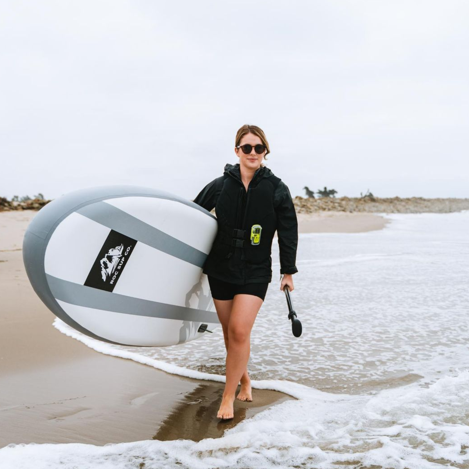 Paddleboardeuse portant un personal locator beacon ACR ResQLink View RLS fixé à sa veste sur une plage.